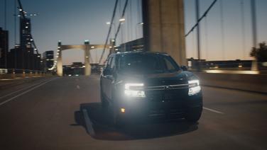 A Ford Maverick driving over a bridge at dusk.