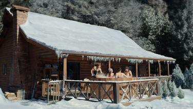 A group of young men and women in a hot tub outside of a house and landscape covered in a foot of snow.