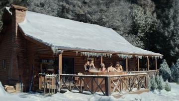 A group of young men and women in a hot tub outside of a house and landscape covered in a foot of snow.