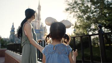 A woman and her young child seen from behind looking up at the castle at Disney Land.