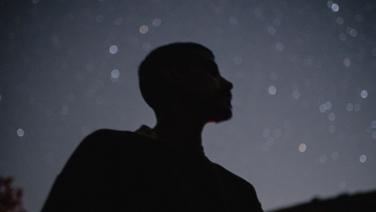 The silhouette of a young man looking up at a starry night sky.