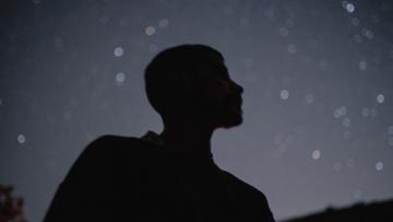 The silhouette of a young man looking up at a starry night sky.