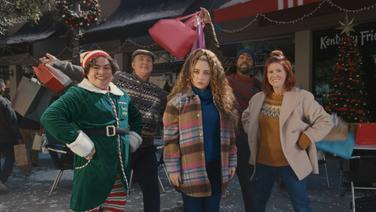A group of people standing outside wearing sweaters and coats smiling and holding gift bags.