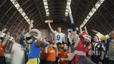 A room full of athletes, mascots, sports fans, and Little Caesar's employees cheering.