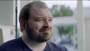 A balding overweight middle-aged white man with a beard and a smirk looking off into the distance.