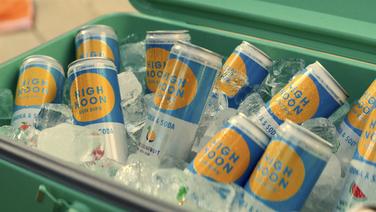 A green cooler full of ice and cans of passion fruit-flavored High Noon Vodka and Soda.
