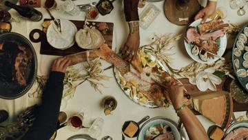 Three hands reaching toward a table full of various food dishes seen from above.