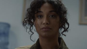 A young black woman with long curly hair and a displeased look on her face.
