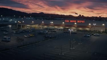 An image of a Home Depot store and parking lot with mountains and a city in the background at sunrise.