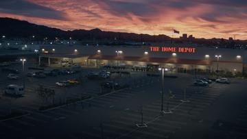 An image of a Home Depot store and parking lot with mountains and a city in the background at sunrise.