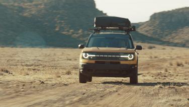 A Ford Bronco SUC with a roof tent driving through the desert.