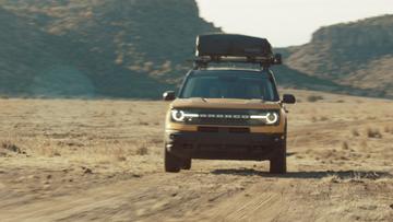 A Ford Bronco SUC with a roof tent driving through the desert.