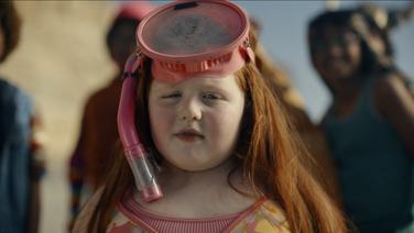 A chubby young white girl with red hair and a swim suit wearing a snorkeling mask.