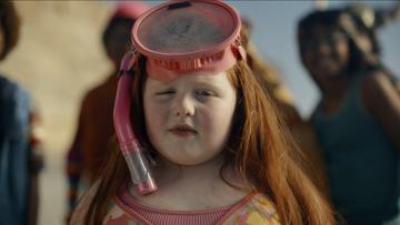 A chubby young white girl with red hair and a swim suit wearing a snorkeling mask.