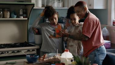A black mother and her two teenage daughters taking a selfie in their kitchen.